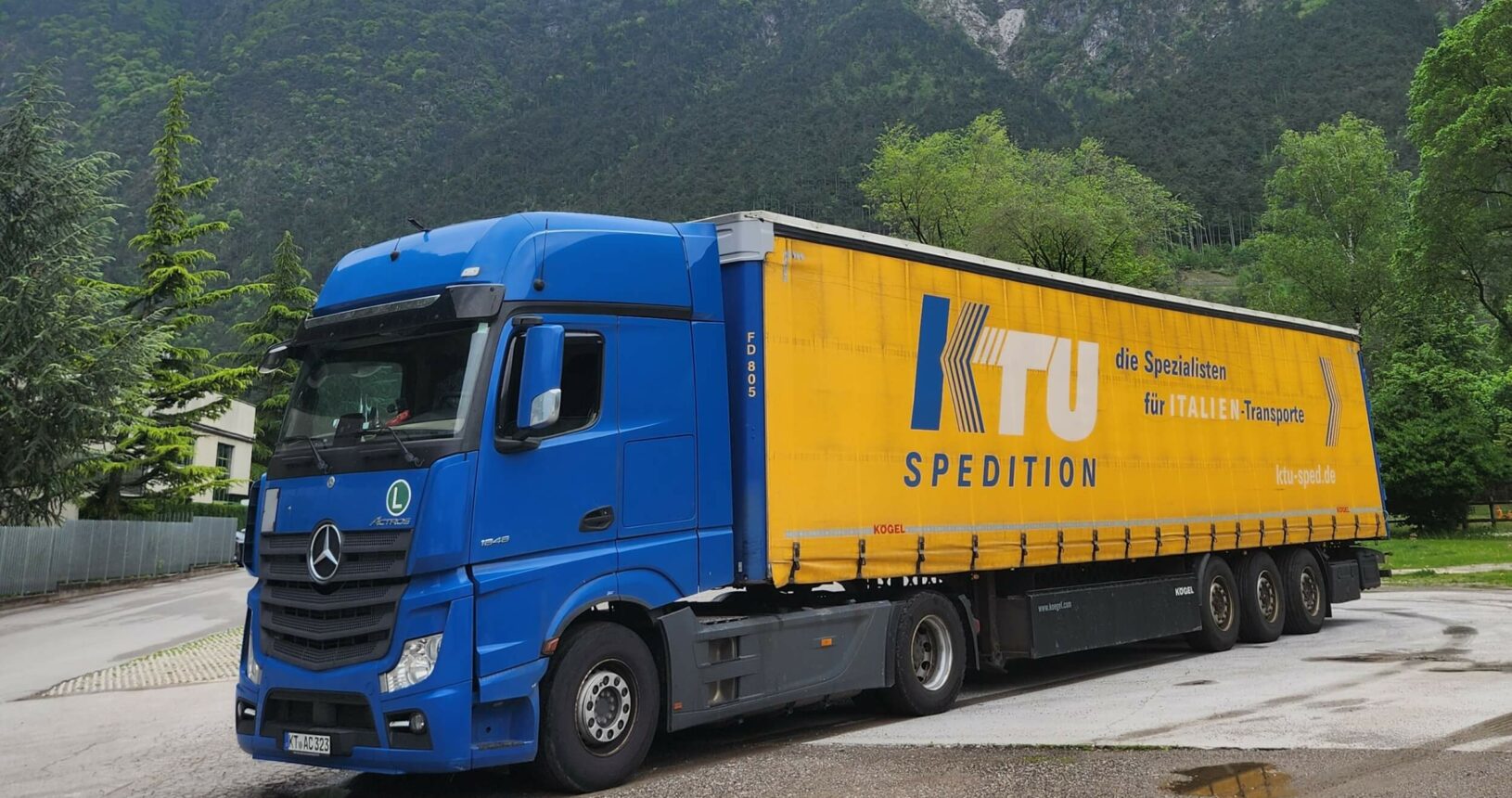 Sattelzug der KTU Spedition auf Parkplatz in Alpenregion an wolkenverhangenem Tag.